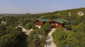 Un grupo de cabañas de madera con techos verdes, rodeadas de abundante vegetación y un cielo despejado.
