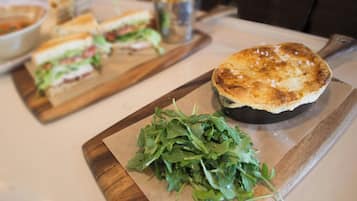 Un sándwich sobre una tabla de madera, un tazón de ensalada y un trozo de carne a la parrilla en un plato.