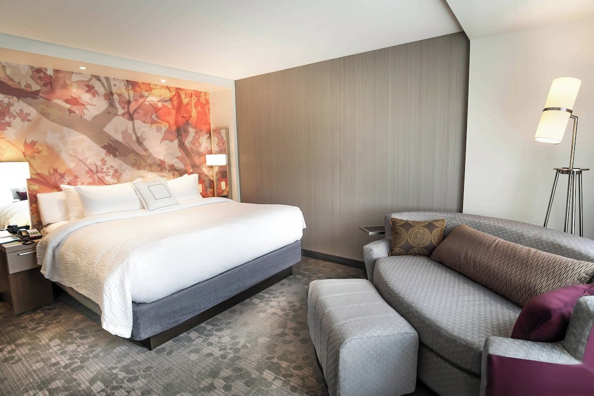A hotel room with a large bed, a sofa, a nightstand with a lamp, and a wall with a leaf pattern.