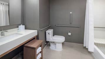 Ein modernes Badezimmer mit weißem Waschbecken, WC und Badewanne. Es gibt einen Holztisch mit Handtüchern und einem Spiegel.