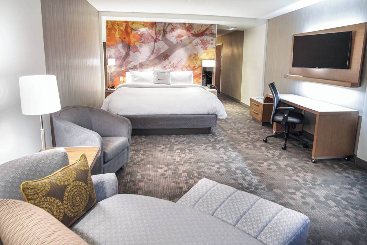 A hotel room with a bed, a desk, a chair, a sofa, and a TV.