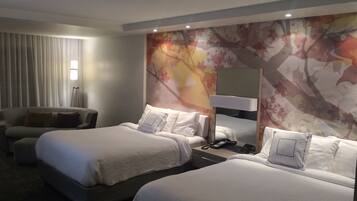 A hotel room with two beds, a sofa, a lamp, and a large mirror.