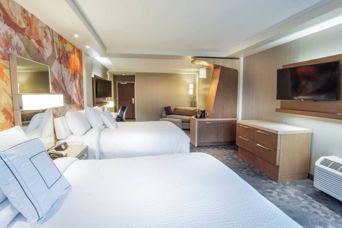 A hotel room with two beds, a desk, a TV, and a large mirror.