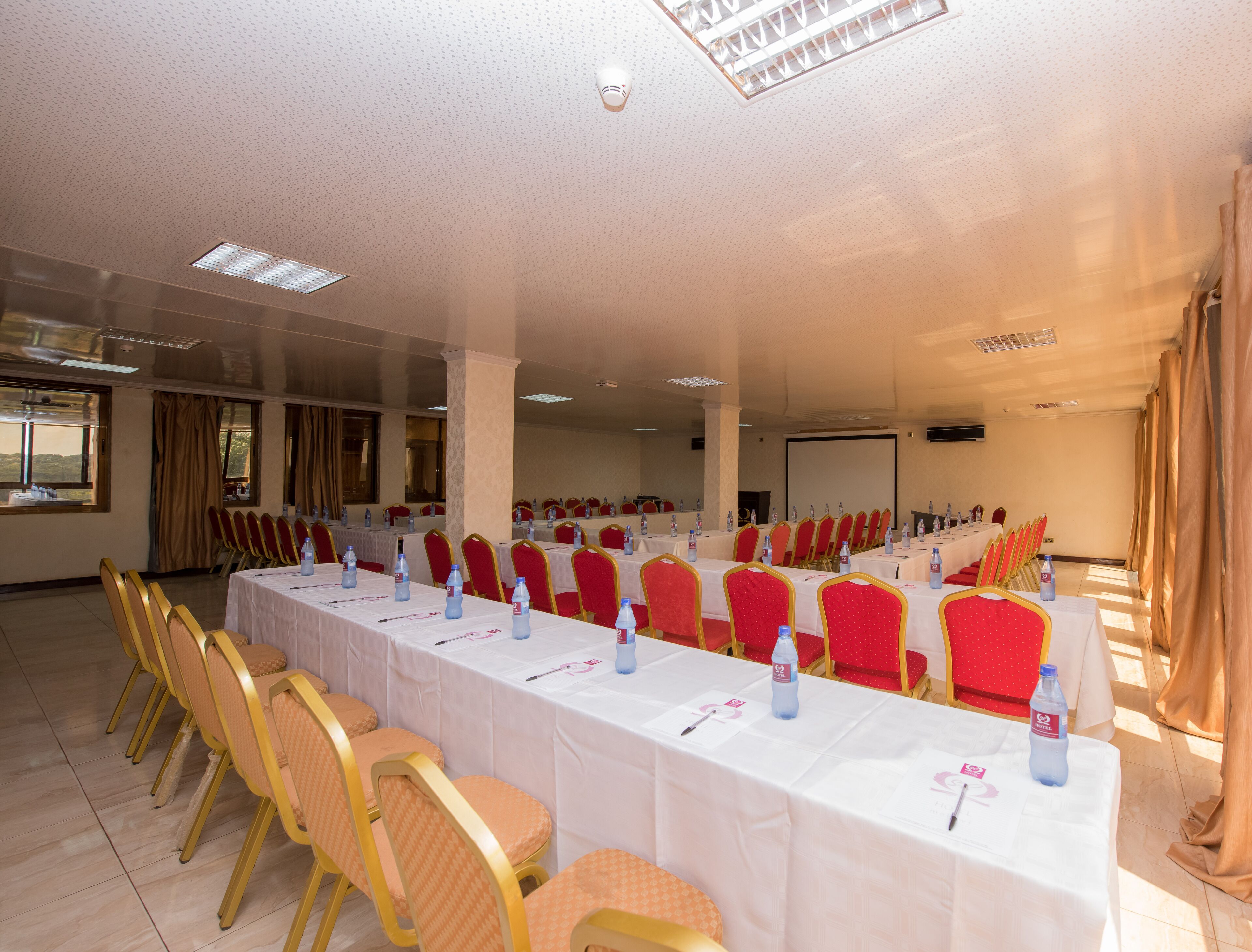 Un salón de conferencias con filas de mesas y sillas, equipado con botellas de agua y tarjetas de identificación.