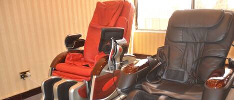A massage chair with a red cover and a black leather chair in a room with striped wallpaper.