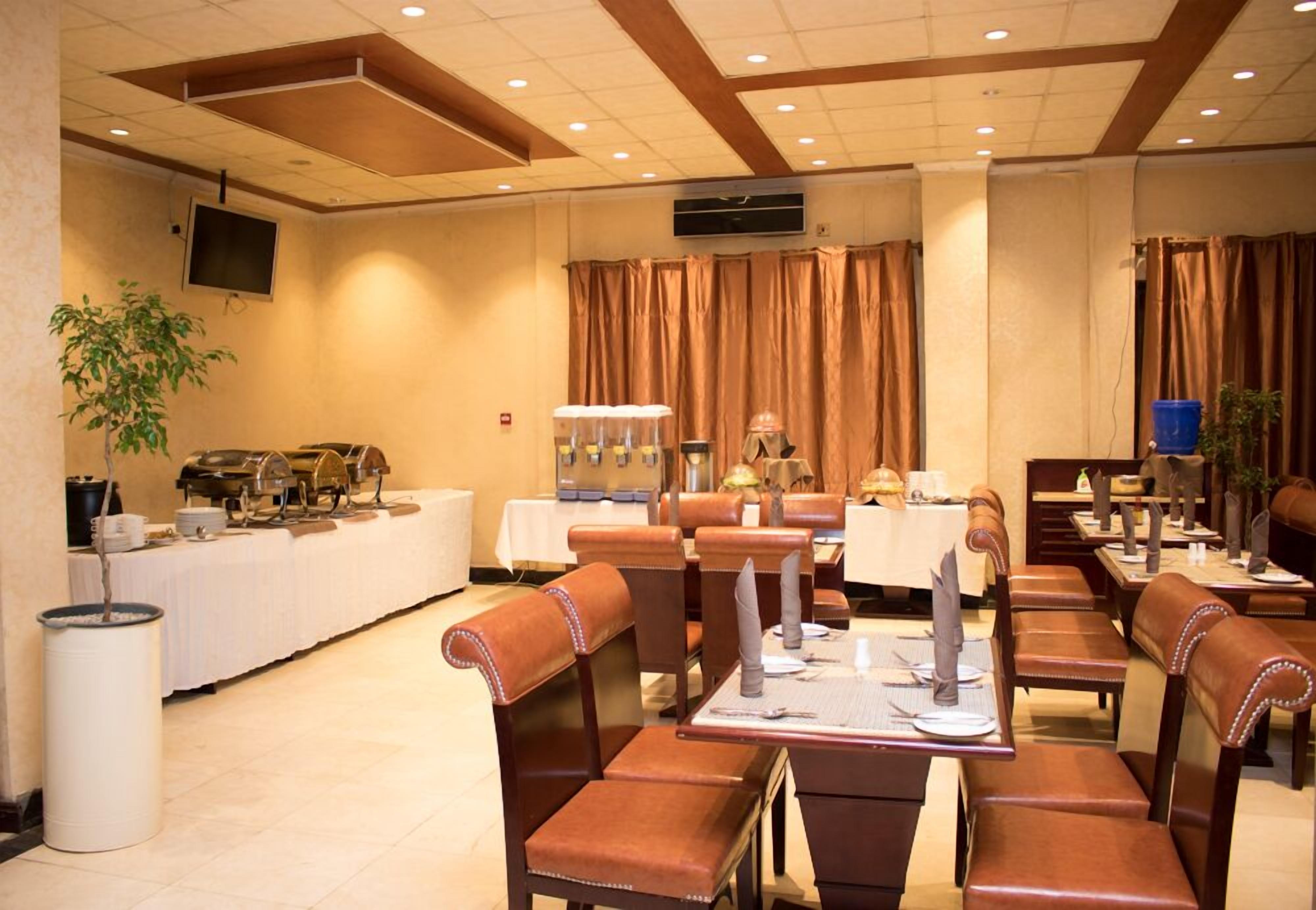 A hotel dining area with leather booths and tables, a buffet line, and a television on the wall.