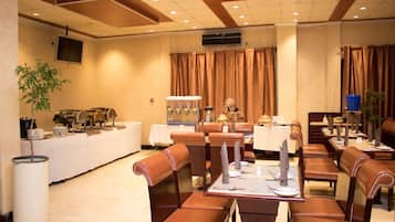 A hotel dining area with leather booths and tables, a buffet line, and a television on the wall.