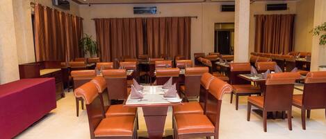 A spacious dining area with multiple tables and chairs, a red counter, and brown curtains.