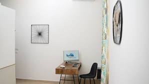 A compact living space with a wooden desk, a computer, a small table with a plant, and a green chair. - Napoli City Rooms (Naples)