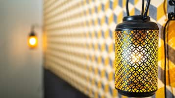 A hanging lantern with a geometric pattern, a wall with a checkered design, and a blurred light source in the background.