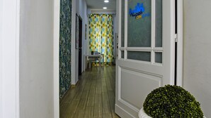 A hallway with a wooden floor, a white door with frosted glass panels, and a white pedestal with a green plant. - Napoli City Rooms (Naples)