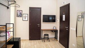 A small, tidy room with a desk, two doors, a TV, and a mirror. - Napoli City Rooms (Naples)