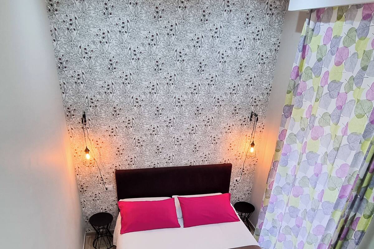 Un dormitorio con una cama, pared estampada, suelo de madera y una cortina.