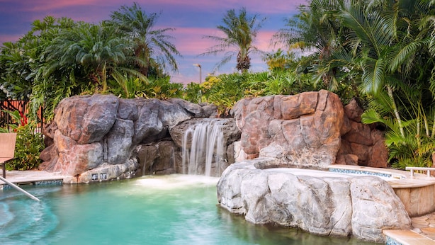 A pool with a waterfall, surrounded by large rocks and palm trees. - Embassy Suites By Hilton Oahu Kapolei (Kapolei)