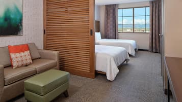 A hotel room with a sofa, two beds, a wooden partition, and a view of the sky.