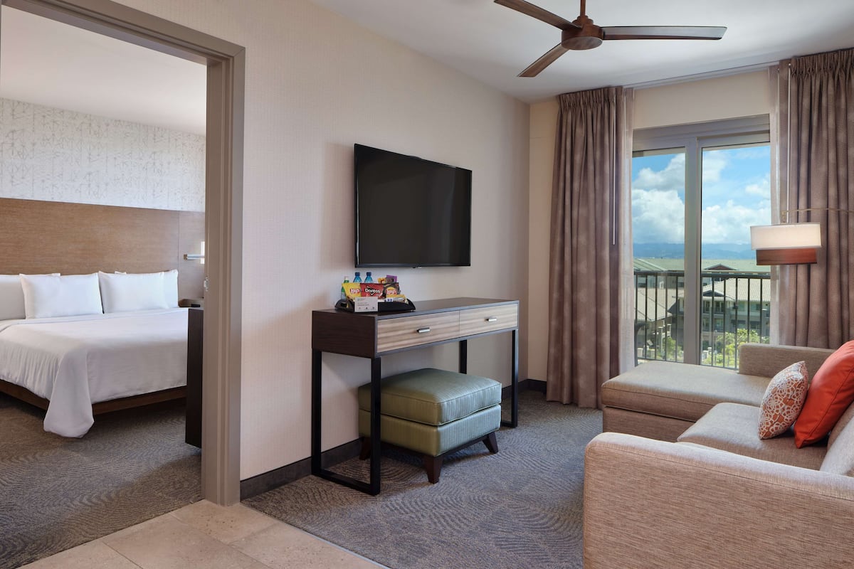 Een hotelkamer met een bed, een bureau met een flatscreen-tv, een bank en een balkon met uitzicht.