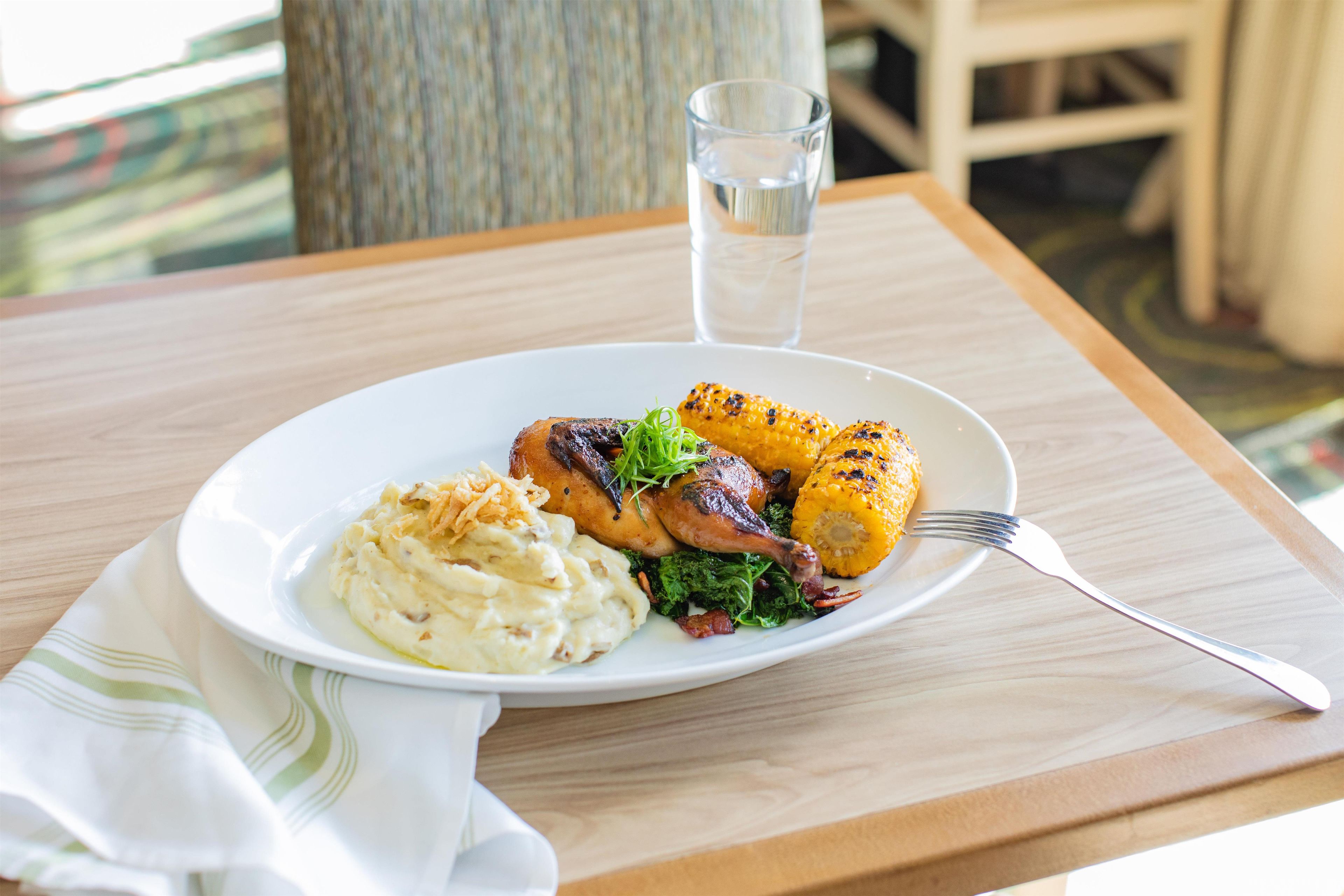 A plate of food with mashed potatoes, grilled chicken, and corn on a wooden table.