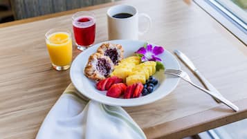 Un piatto per la colazione con frutta, un dolce e una tazza di caffè su un tavolo di legno.