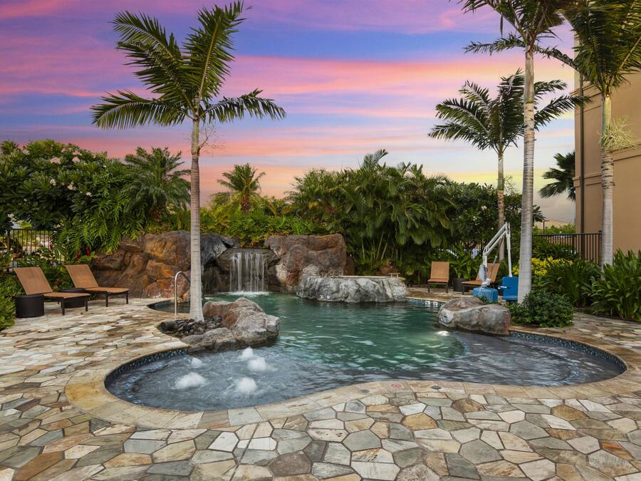 A pool area with a waterfall, lounge chairs, and tropical plants.