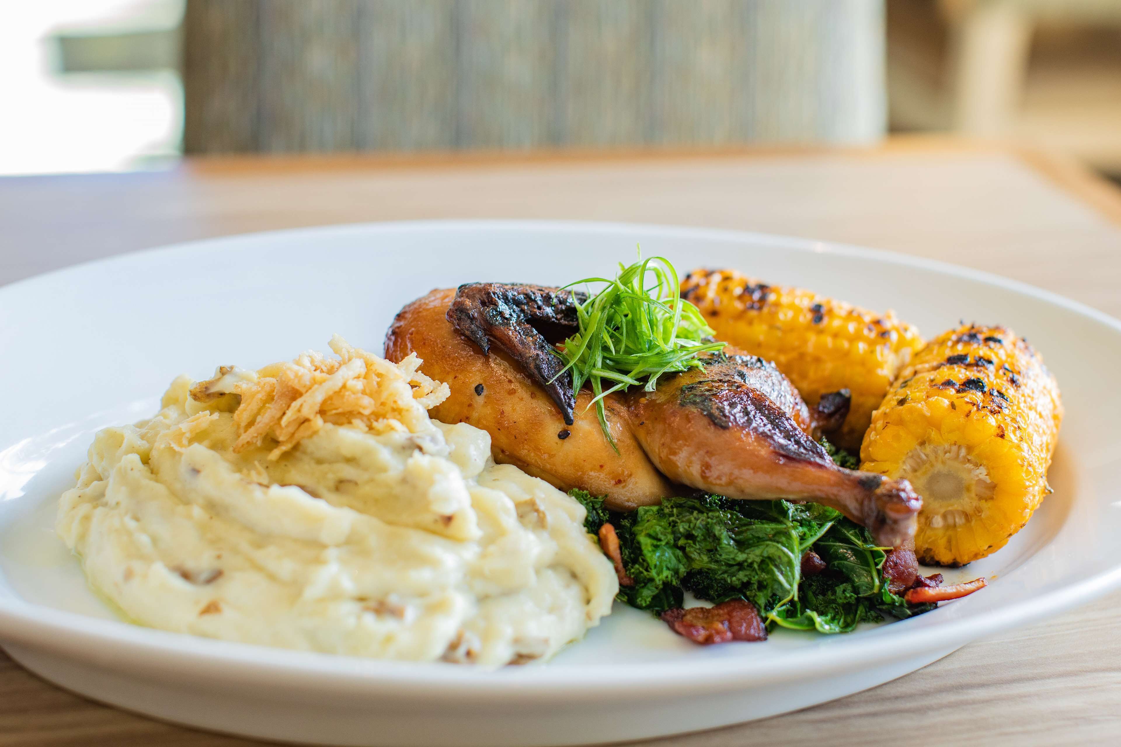 A plate of food with mashed potatoes, roasted chicken, and grilled corn on a white plate.