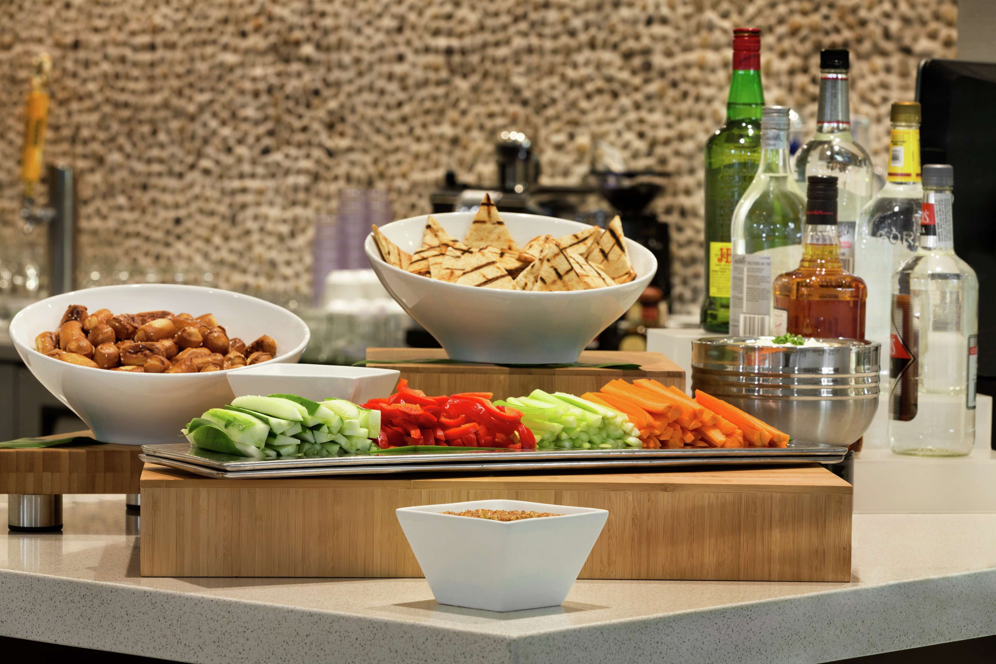 A buffet table with various food items and condiments, including bowls of nuts, vegetables, and a bowl of chips.