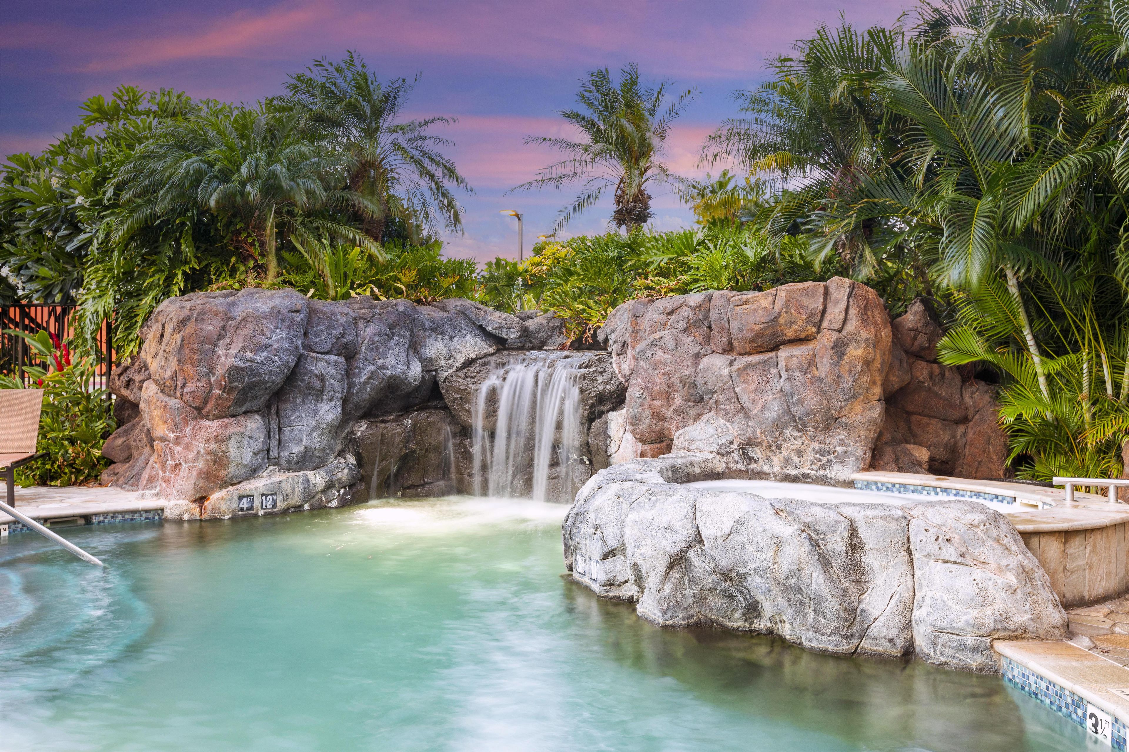 A pool with a waterfall feature surrounded by tropical vegetation.