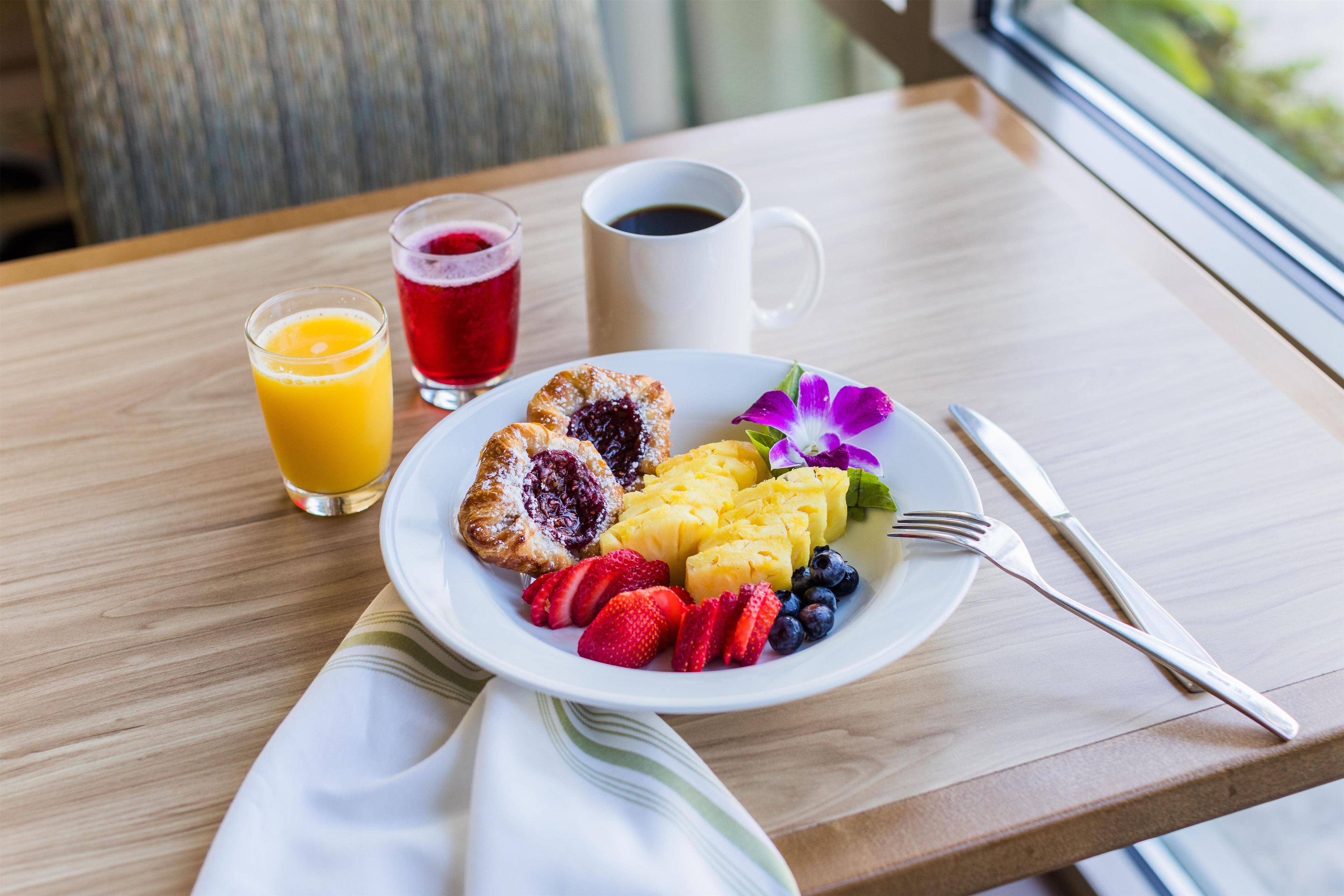 A breakfast plate with fruit, a pastry, and a cup of coffee on a wooden table.