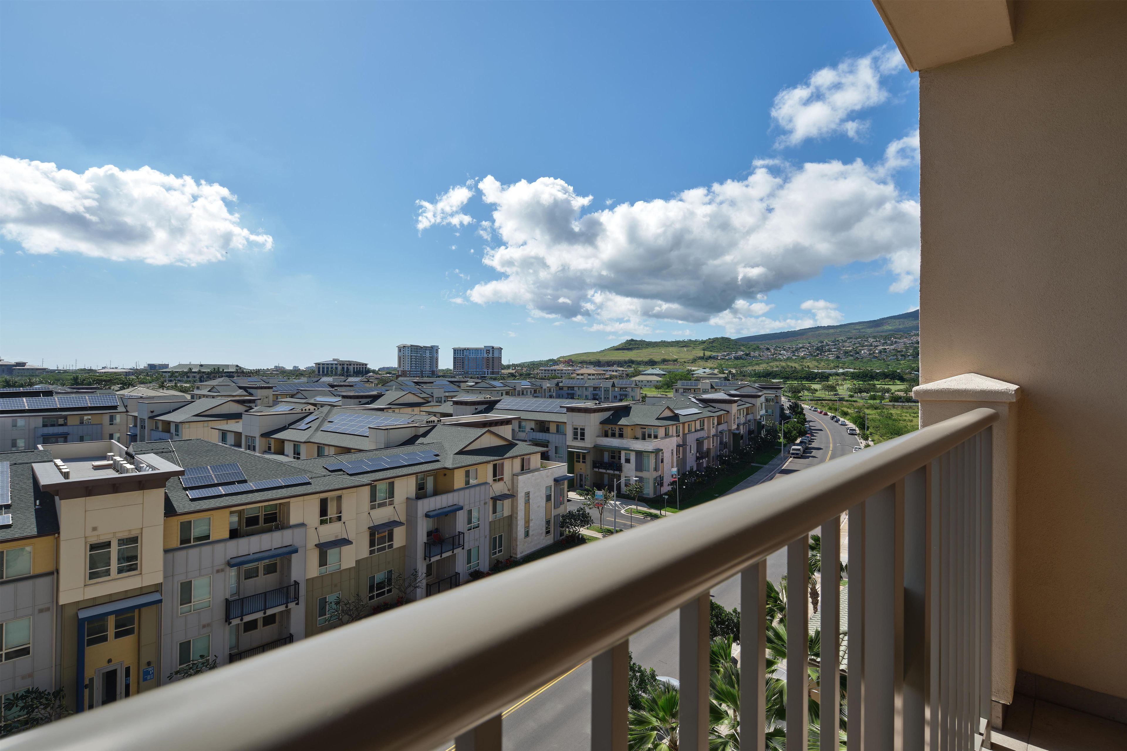 A residential area with multiple-story buildings, a clear sky, and a distant view of a hilly landscape.