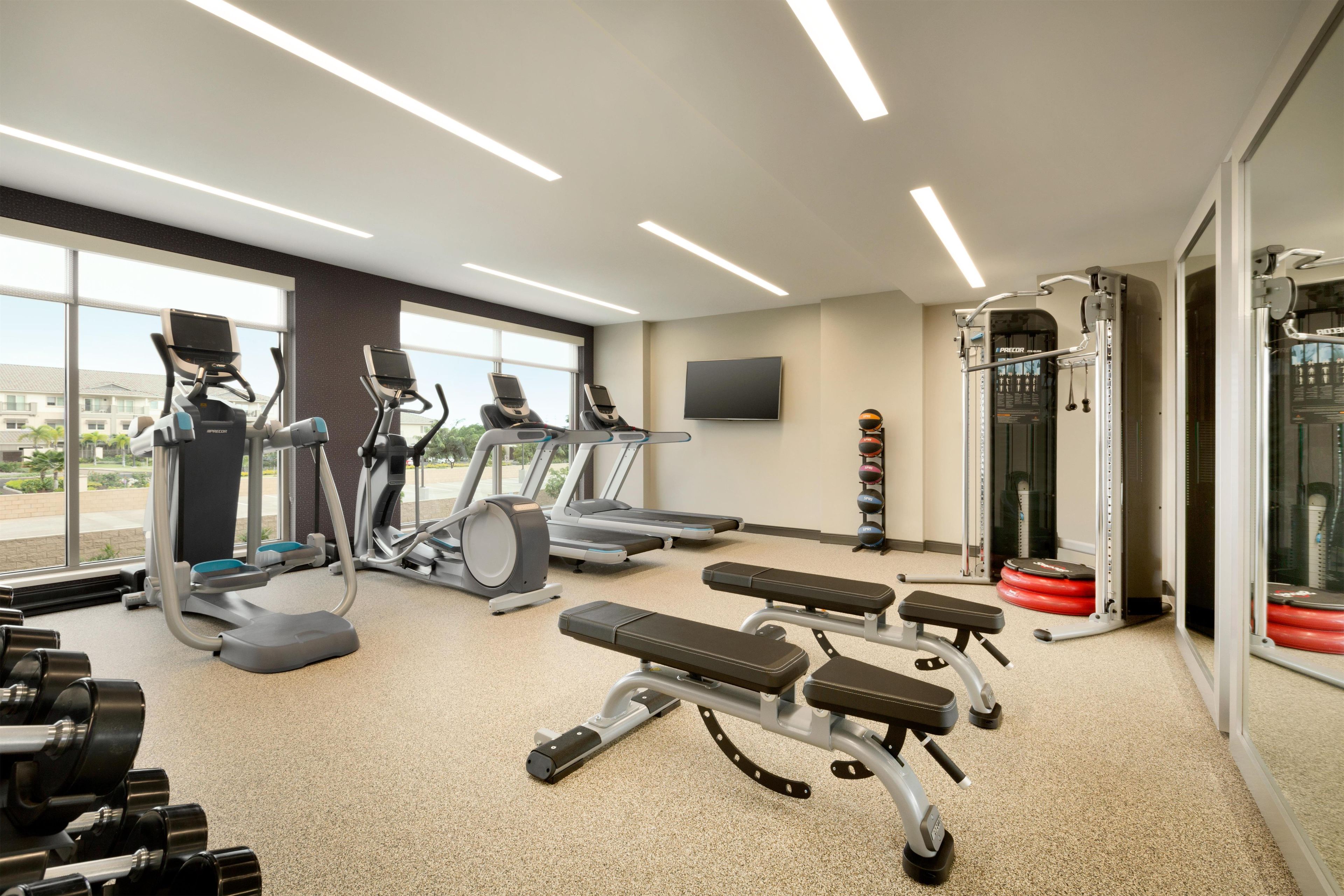 Un gimnasio con cintas de correr, elípticas, una prensa de banca y una zona de levantamiento de pesas.