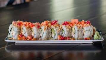 A plate of sushi rolls with various toppings and a small dollop of wasabi on a dark wooden table.