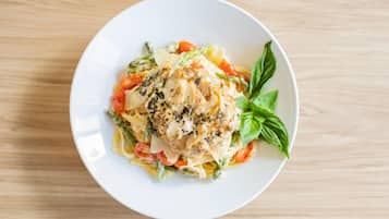 A white plate with pasta, chicken, and vegetables on a wooden table.