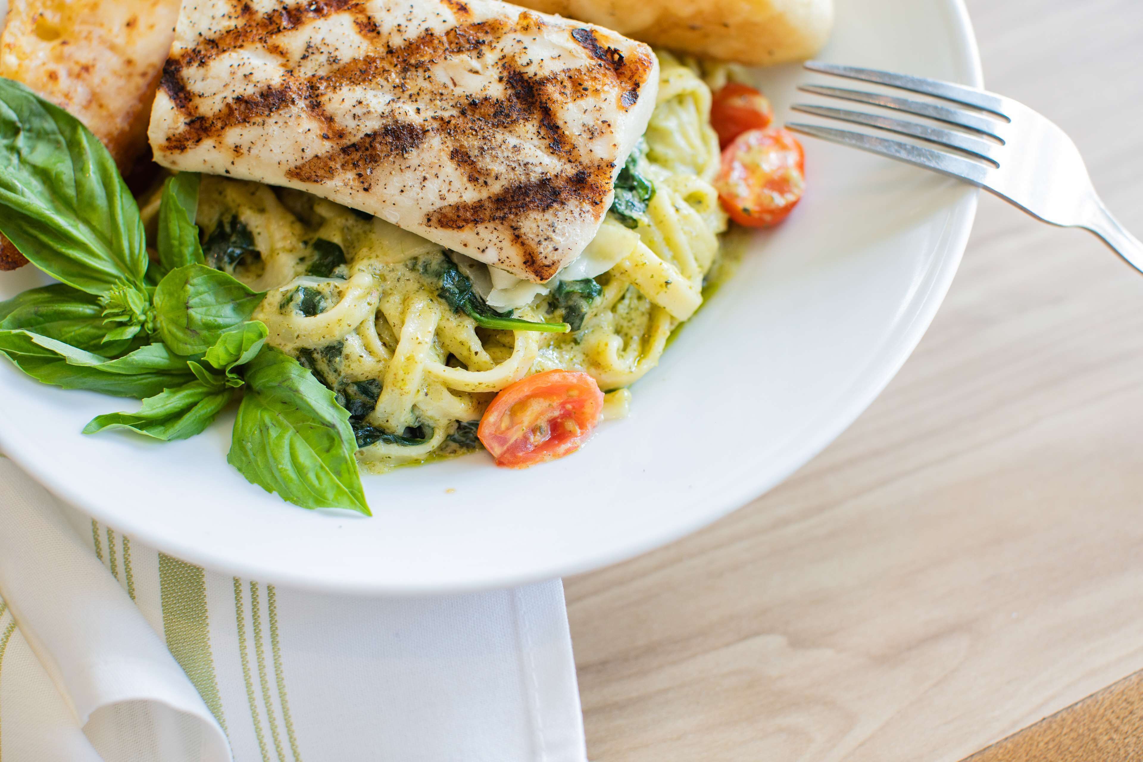Un plato de comida con pescado a la parrilla, pasta y albahaca fresca.