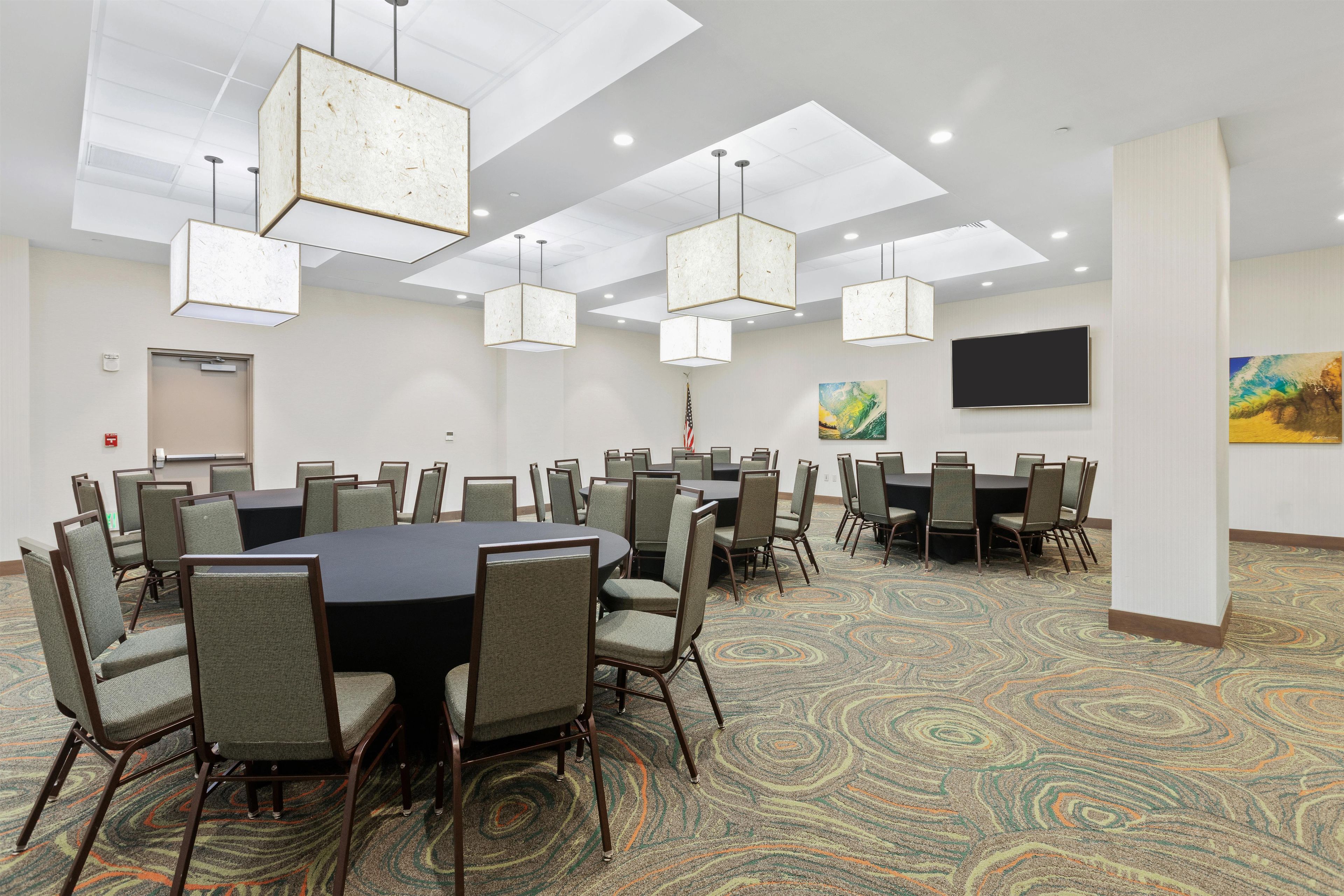 A conference room with a large round table, multiple chairs, pendant lighting, a flag, and a painting on the wall.