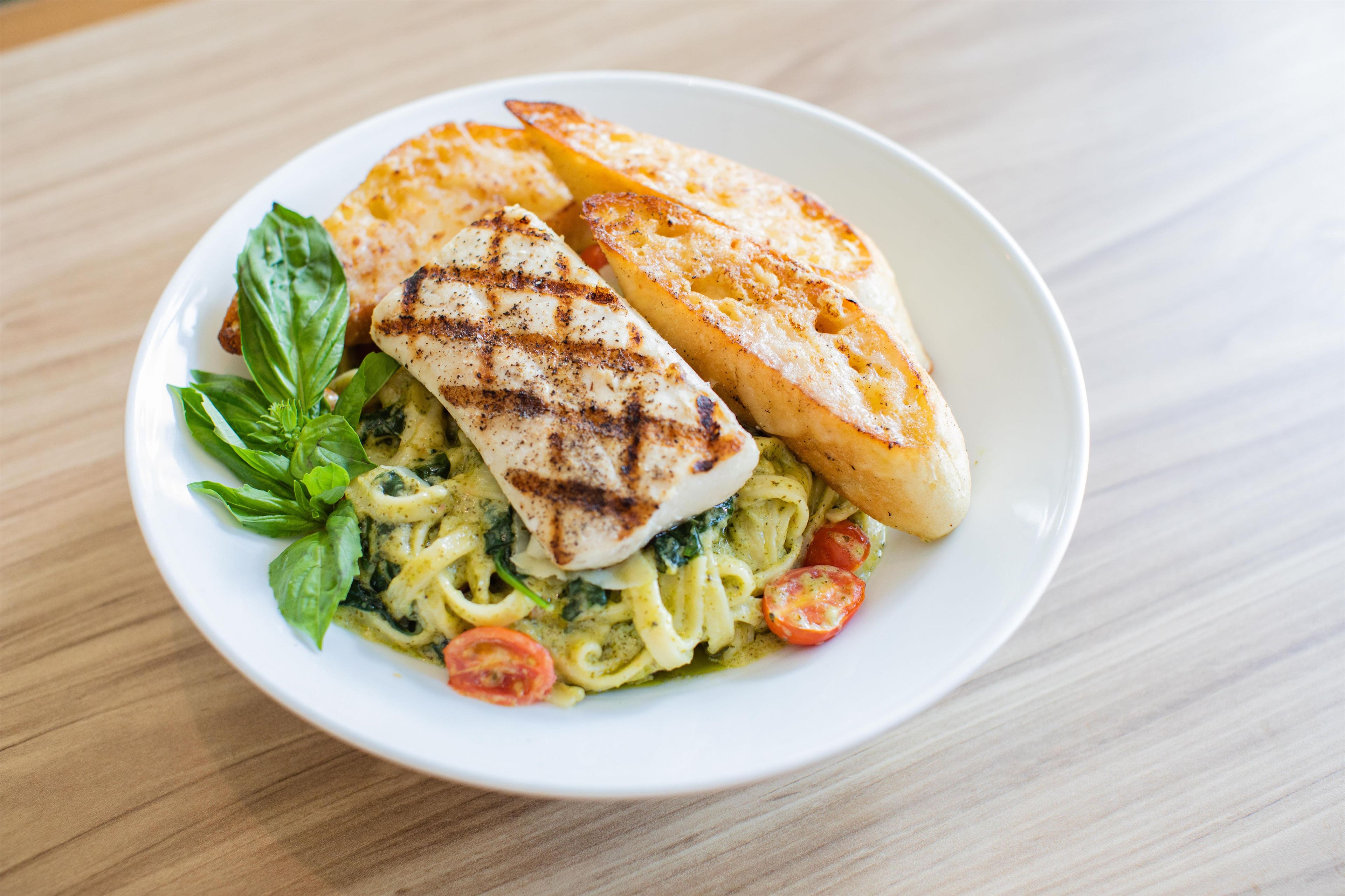 Een bord pasta met gegrilde kip, tomaten en basilicum.