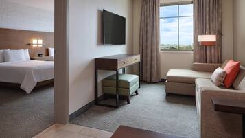 Una habitación de hotel con cama, escritorio, televisor, sofá y ventana con cortinas.