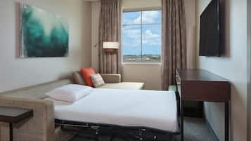 A hotel room with a bed, a desk, a chair, a TV, and a window with curtains.