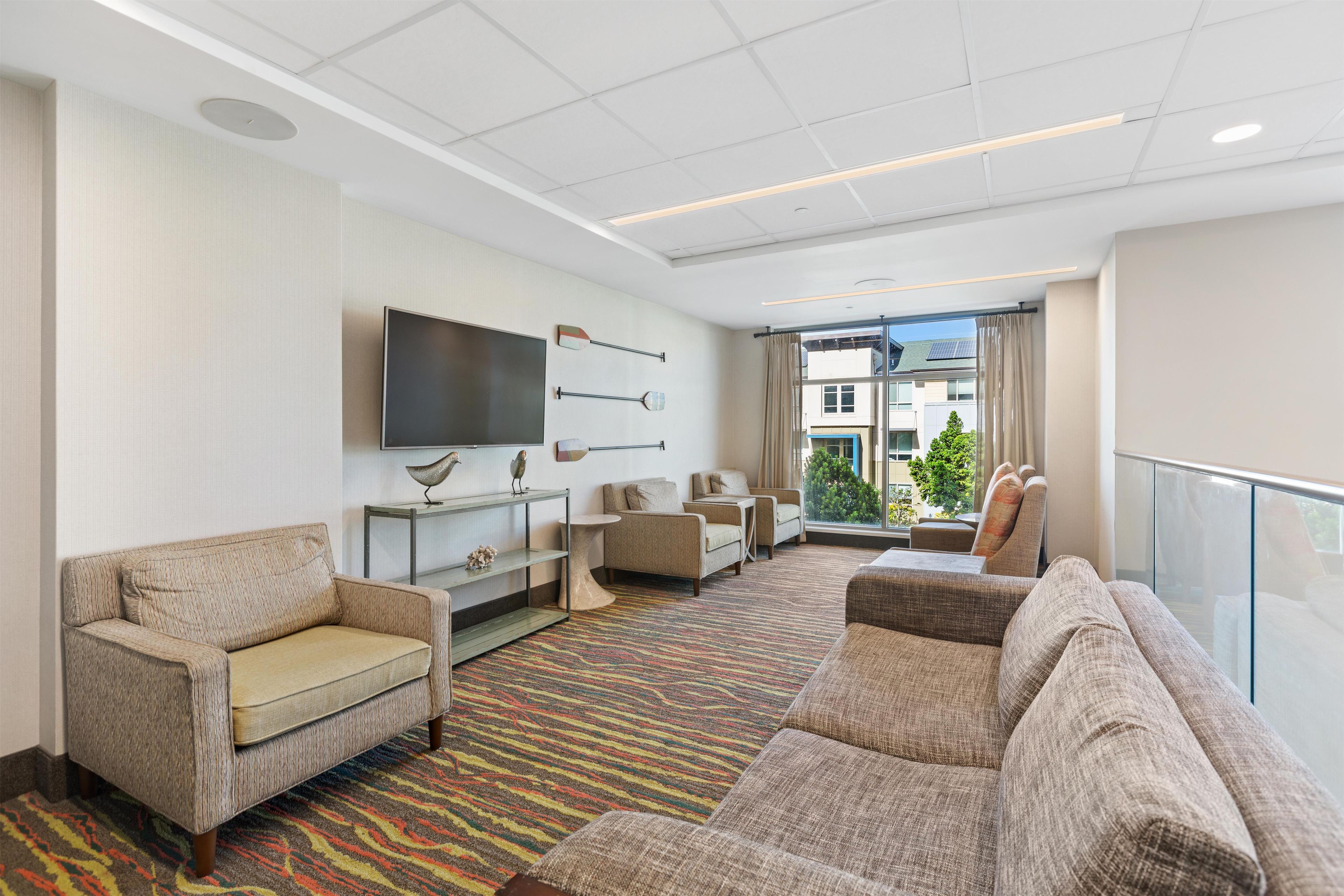 A hotel lobby with a sofa, chairs, a flat-screen TV, decorative wall art, and a view of the outside.