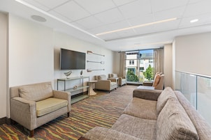 A hotel lobby with a sofa, chairs, a flat-screen TV, decorative wall art, and a view of the outside.