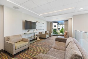 A hotel lobby with a sofa, chairs, a flat-screen TV, decorative wall art, and a view of the outside.