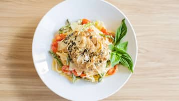 Un plato blanco con pasta, pollo, espárragos y tomates sobre una mesa de madera.