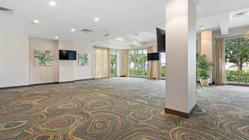 A spacious room with a patterned carpet, large windows, and a flat-screen TV mounted on the wall.