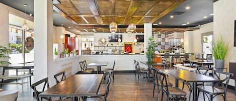 A restaurant interior with wooden tables and chairs, a bar area, and a large TV screen.