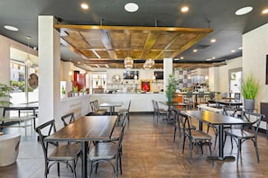 A restaurant interior with wooden tables and chairs, a bar area, and a large TV screen.