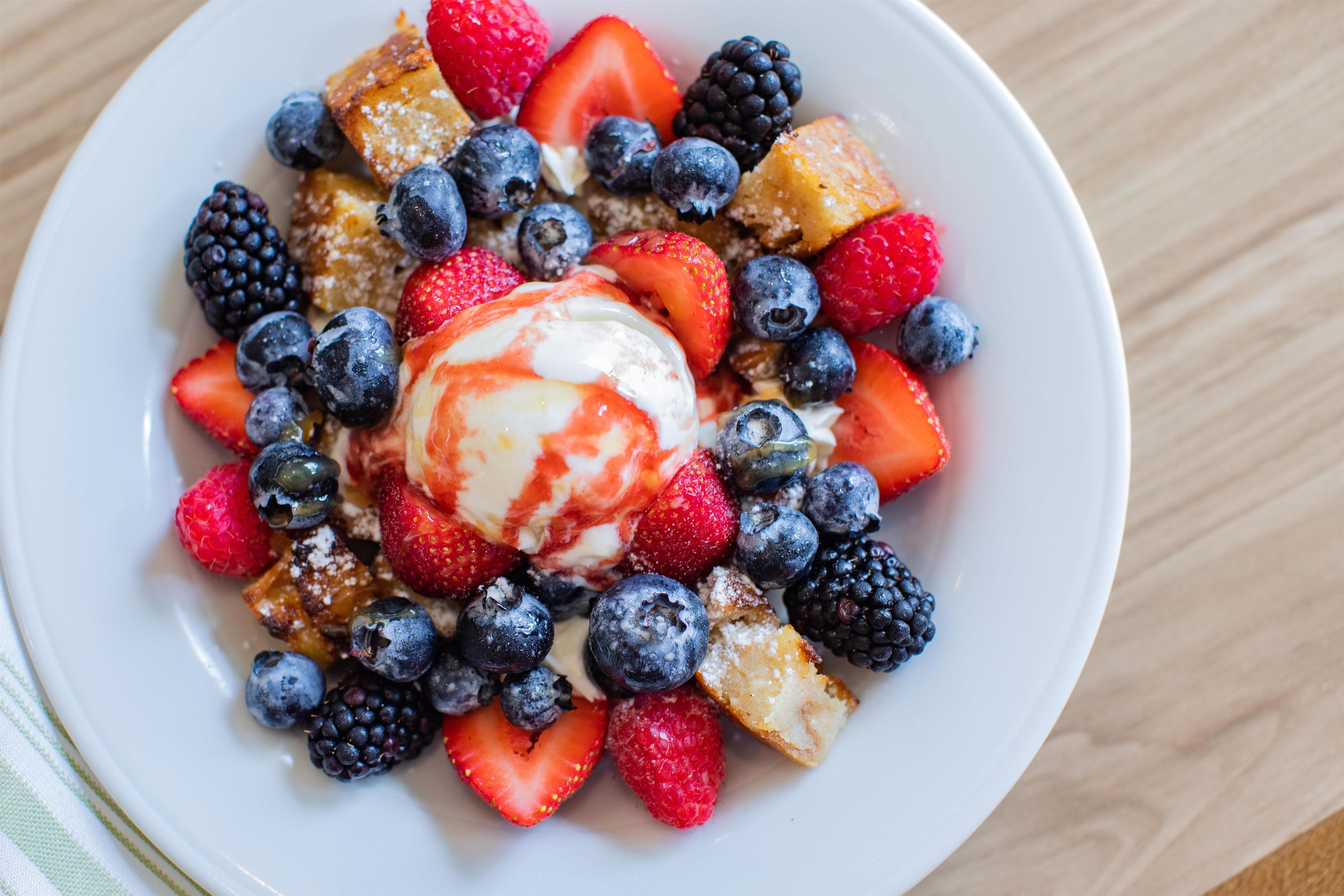 A plate of food with strawberries, blueberries, blackberries, and a scoop of ice cream.