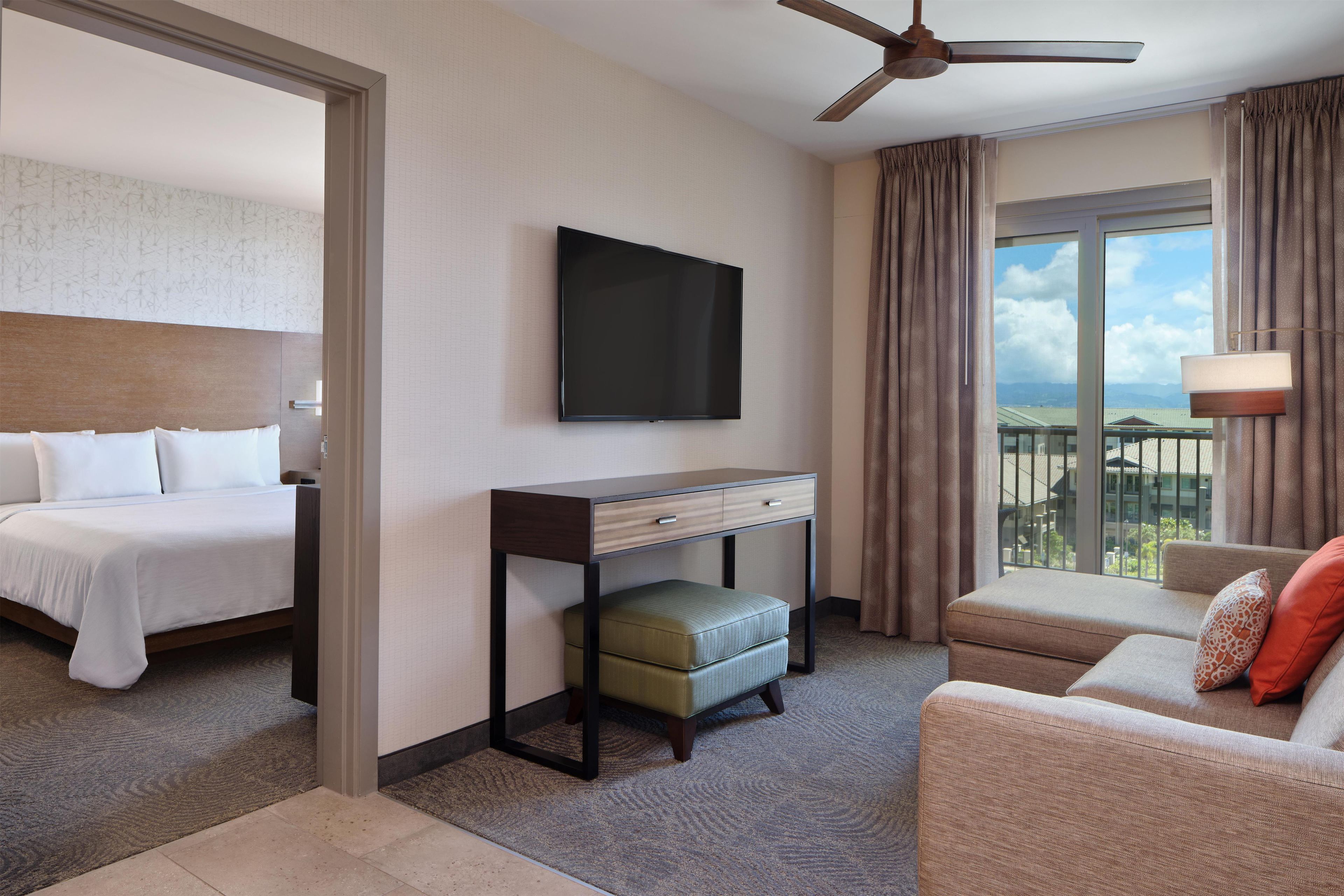 Una habitación de hotel con cama, escritorio, televisor, sofá y balcón con vistas.