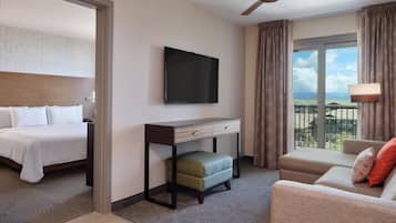 Una habitación de hotel con cama, escritorio, televisor, sofá y balcón con vistas.