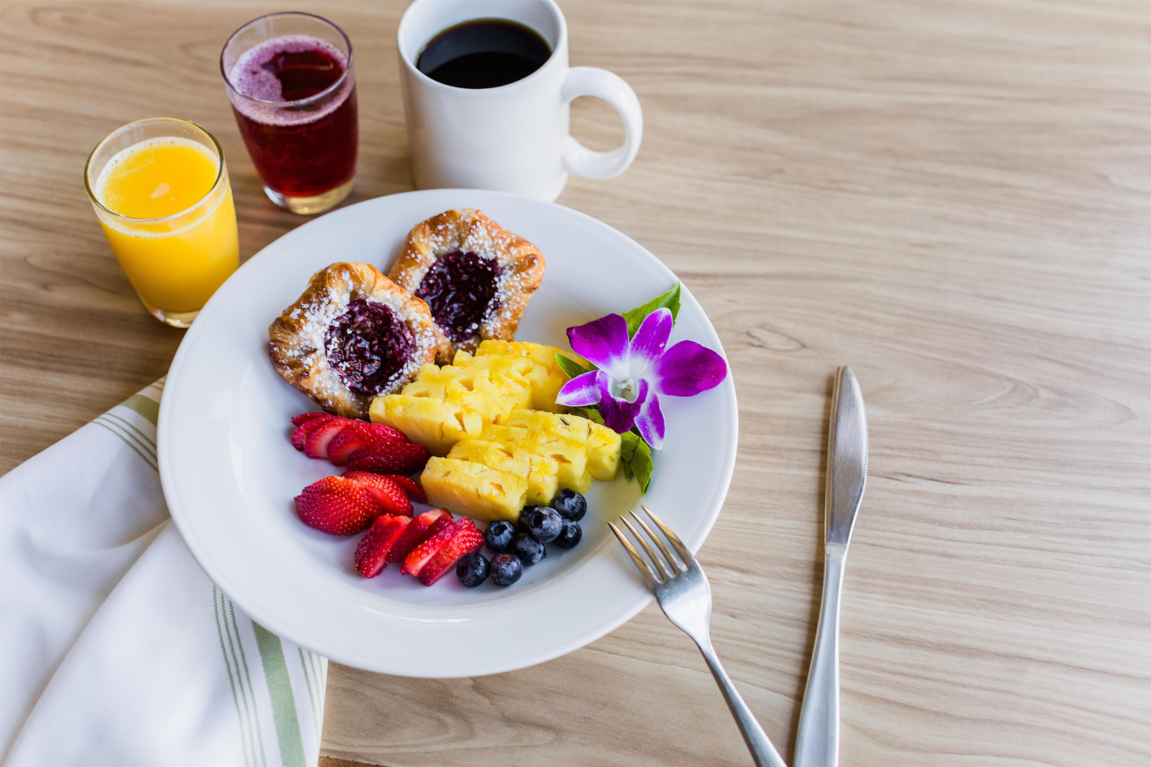 Ein Teller mit Obst und Gebäck auf einem Holztisch, dazu eine Tasse Kaffee und ein Glas Orangensaft.