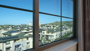 A residential area with multiple houses, some with solar panels, viewed through a window with a view of a hilly landscape.