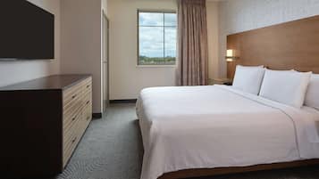 Une chambre d’hôtel comprenant un lit, une commode, une télévision, une fenêtre avec des rideaux et une table de chevet avec une lampe.