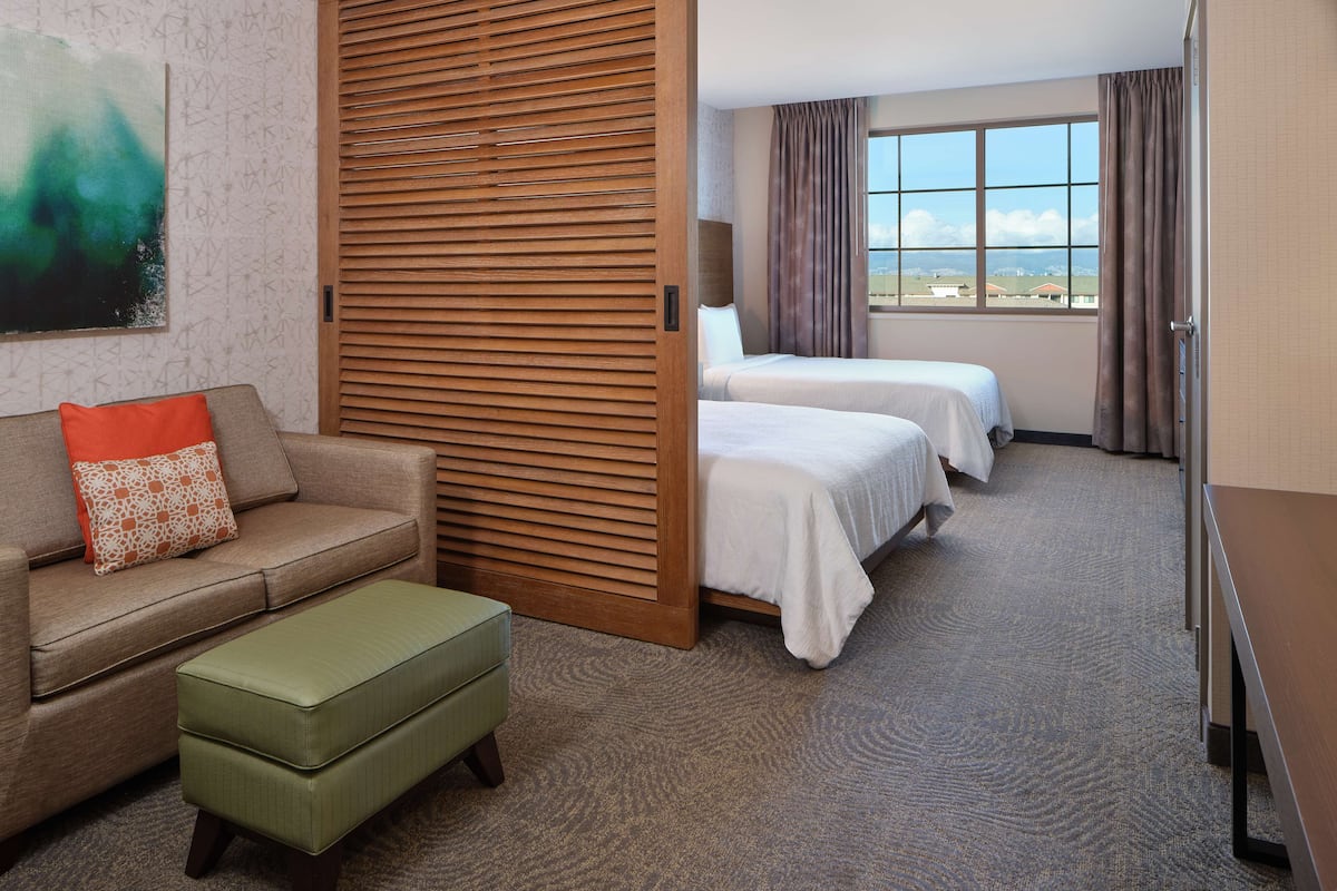 Een hotelkamer met een bank, twee bedden, een houten scheidingswand en een groot raam met uitzicht.